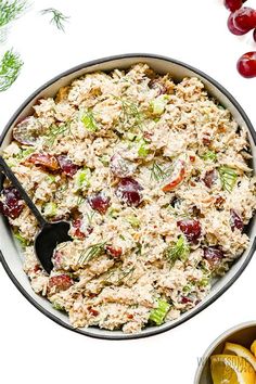 a bowl filled with chicken salad next to lemons and cherries on a white surface