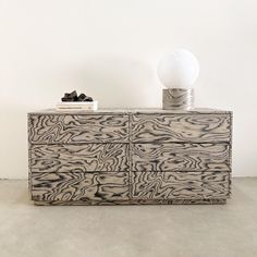 a white lamp sitting on top of a wooden dresser next to a black and white object