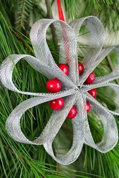 a christmas ornament hanging from a pine tree with red berries and silver ribbon