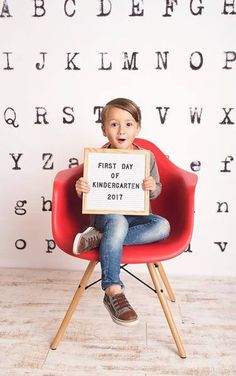 a little boy sitting in a red chair holding a sign