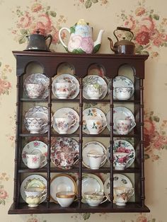 an old china cabinet with plates and cups on it in front of a floral wallpapered wall