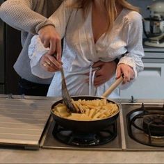 two women are preparing food in a pan on top of the gas stove, one is holding a ladle