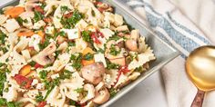 a plate full of pasta with chicken, carrots and spinach on it next to a gold spoon