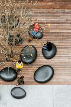 two people sitting on black rocks in the middle of a wooden deck with a tree