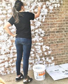 a woman standing in front of a brick wall with her hand on the paint bucket