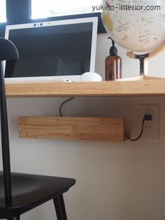 a computer monitor sitting on top of a wooden shelf next to a black chair and desk lamp