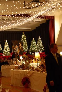 a man standing in front of a table covered with christmas trees and presents under lights