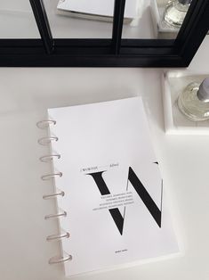 an open notebook sitting on top of a white table next to a mirror and other items