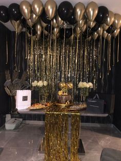 gold and black balloons are hanging from the ceiling above a table with a cake on it