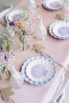 the table is set with plates and vases filled with flowers, seashells and starfish