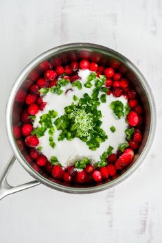 a pot filled with red berries and green garnish on top of a white table