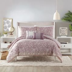 a bed with pink comforter and pillows in a room next to a white dresser