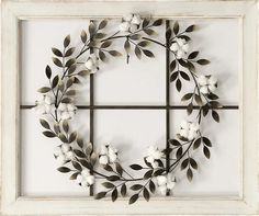 a wreath made out of branches and flowers on a white wall hanging in front of a window