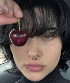 a woman with piercings and an apple on her nose is holding up a piece of fruit