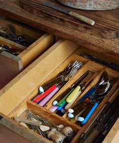 an open drawer with utensils and spoons in it on top of a wooden table