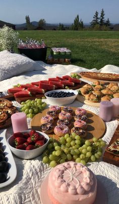 a table filled with lots of food on top of a white blanket next to a field