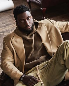 a man sitting on top of a couch wearing a tan coat and khaki pants