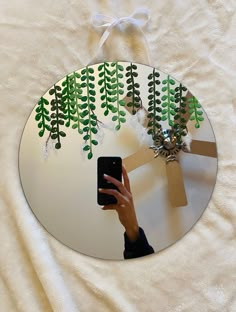 a person holding a cell phone in front of a mirror with green plants on it