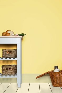 a shelf with baskets and bread on it next to a wall painted in bright yellow