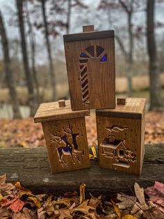 three wooden blocks with designs on them sitting in leaves and trees behind them are the woods