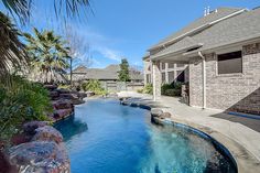 an outdoor swimming pool surrounded by palm trees and rocks with a house in the background