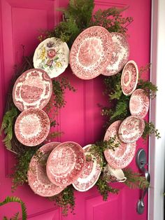 a pink door decorated with plates and greenery