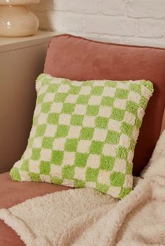 a green and white pillow sitting on top of a brown couch next to a brick wall