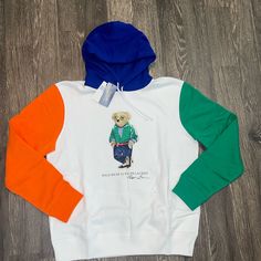 This Polo Ralph Lauren Sweatshirt Features A Unique Combination Of Colors: Crisp White, Green, Orange Sleeves, And A Blue Hood. The Design Showcases The Iconic Polo Bear Accompanied By The Brand's Logo And Crest. The Garment Is Made Of A Cozy Fleece Fabric Composed Of Polyester And Cotton And Is Adorned With Accents That Add To Its Preppy Style. This Sweatshirt Is Perfect For Any Season And Can Be Easily Cared For In A Machine Wash. The Size Is L And The Closure Is Pullover. The Garment Is A Reg Polo Ralph Lauren Hoodie, Polo Ralph Lauren Sweatshirt, Ralph Lauren Hoodie, Distressed Sweatshirt, Ralph Lauren Sweatshirt, Ralph Lauren Boys, Polo Bear, Ralph Lauren Shorts, Vintage Polo Ralph Lauren