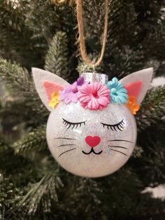 a cat ornament hanging from a christmas tree with flowers on it's head