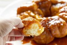 a hand holding up a piece of doughnuts with sauce on the side and other pastries in the background