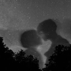 a couple kissing under the stars in the night sky with trees silhouetted against them