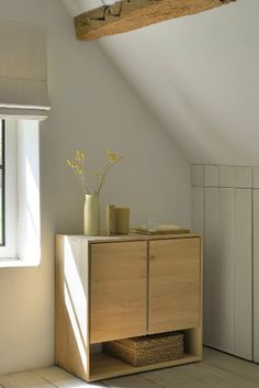 an empty room with white walls and wooden furniture in the foreground is a window