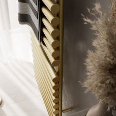 a gold radiator in front of a white wall and a vase with dried flowers