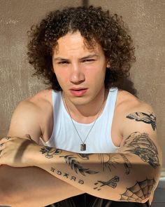 a man with long curly hair and tattoos on his arms is looking at the camera