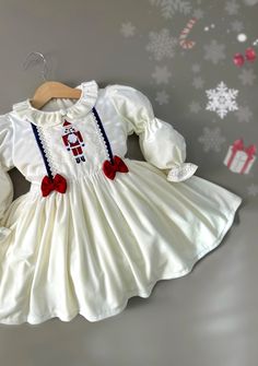 Pearl white velvet dress offers your child elegance and comfort at the same time.The nutcracker embroidery on the front of the dress will amaze you.little red bows, sparkly blue ribbon and other cute accessories add sparkle to the dress Its color and softness make this fabric special from others.Touching it will make you happy. - The inside of the dress is lined with 100% cotton fabric. - Long ties extend from either side of the waist, providing a customizable fit, ideal for growing kids. - Long Christmas Dress For Baby Girl, Christmas Dress For Baby, Nutcracker Embroidery, Girl Nutcracker, White Velvet Dress, Baby Girl First Christmas, Baby Christmas Dress, Velvet Christmas Dress