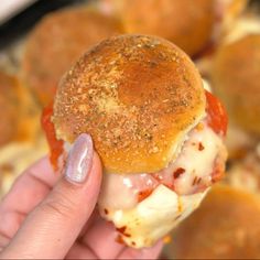 a hand holding a sandwich with meatballs in the background