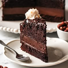 a piece of chocolate cake on a plate with a fork and bowl of nuts in the background