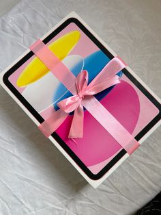 a box with a pink ribbon tied around it on top of a white tablecloth