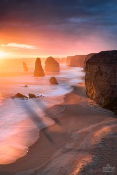 the sun is setting over the ocean with rocks in the water and waves crashing on the beach