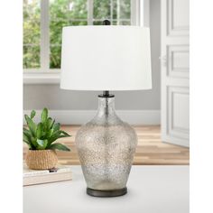 a table lamp sitting on top of a white table next to a potted plant