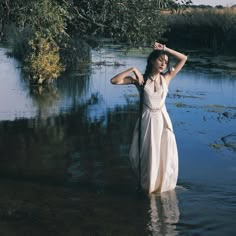 a woman in a white dress is standing in the water with her hands on her head