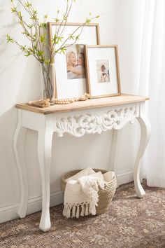 a white table with two pictures on it and a basket next to it in front of a window