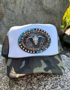 "We are the Proud Original Creator of this Camo cowboy buckle trucker hat! Introducing the epitome of stylish headwear: our exclusive, Original designer of a \"Buckle Patch\" Camo, Otto Brand Trucker Hat. Crafted for the trendsetter who embraces the fusion of edgy and chic, this hat features a unique metal buckle patch of a bull skull adorned with turquoise embellishments and sparkling rhinestones. Each detail exudes individuality and craftsmanship, making it a standout piece in any collection. With a sturdy metal buckle patch, this hat offers both style and functionality, ensuring a perfect fit for every wearer. Be  one of the  very first to own this one-of-a-kind accessory, exclusively available at Hot Off The Press Trends. Grab yours now and make a bold statement wherever you go!   We a Adjustable Western Snapback Hat With Curved Brim, Western Style Adjustable Snapback Hat With Curved Brim, Western Style Adjustable Curved Brim Snapback Hat, Trucker Hat With Curved Brim For Country Events, Adjustable Trucker Cap For Rodeo, Western Snapback Hat For Outdoor, Western Style Outdoor Snapback Hat, Western Style Adjustable Snapback Hat, Western Snapback Trucker Hat For Ranch