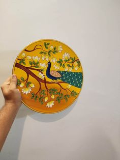 a hand holding a yellow plate with a peacock painted on it