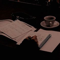 a person sitting at a table with a notebook and pen in front of them, next to a cup of coffee