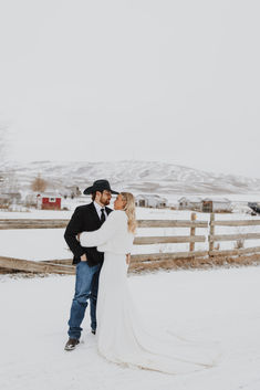 a bride and groom standing in the snow by a fence at their ranch wedding venue