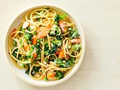 a white bowl filled with pasta and veggies on top of a wooden table