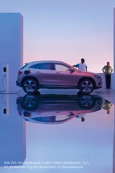 two people standing next to a car in the middle of a room with mirrored floors