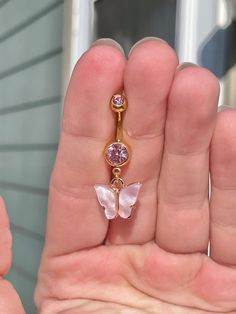 a person holding a pink and gold butterfly belly button ring in their left hand,