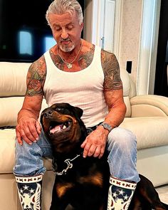 a man sitting on top of a couch next to a black and brown dog wearing cowboy boots